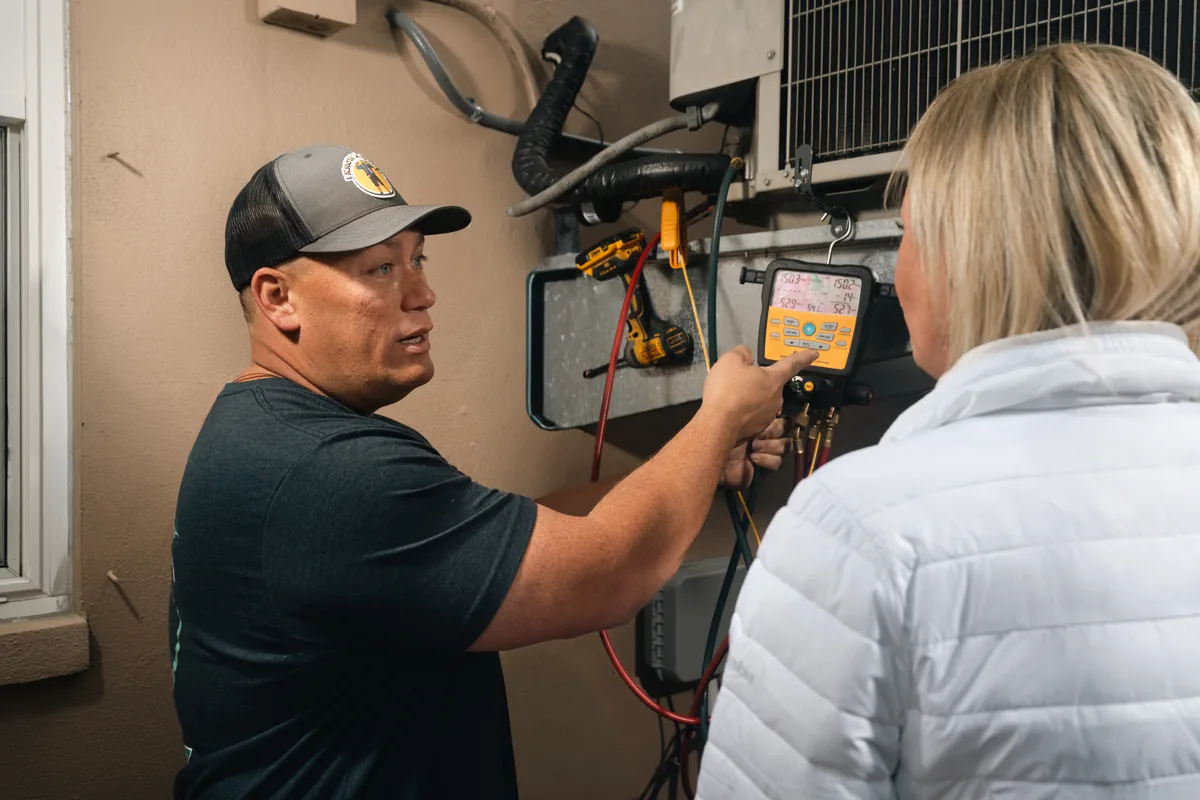 An I Know A Guy AC technician showing a homeowner the digital gauge readings on her system