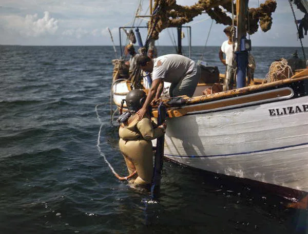 Historic color photo of a Greek sponge diver in a brass diving helmet on the edge of a boat at Tarpon Springs