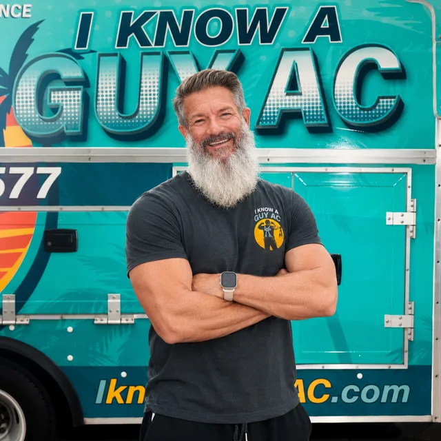 I Know A Guy AC technician standing in front of the branded turquoise truck