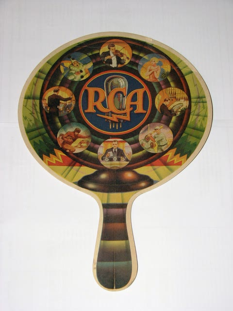 A colorful printed cardboard advertising hand fan on a wooden stick, of the kind given away by stores and funeral homes in the 1920s.