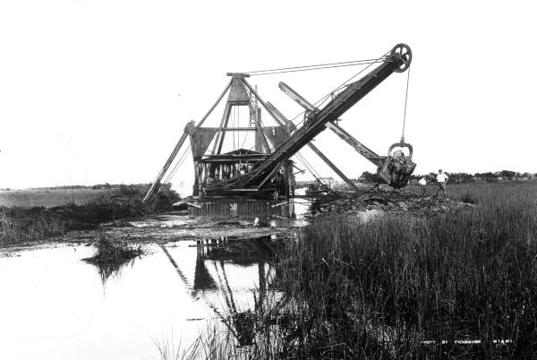 A floating dredge at work in a Florida waterway in 1921, its boom and pipe throwing dredged spoil to one side to build up dry ground.
