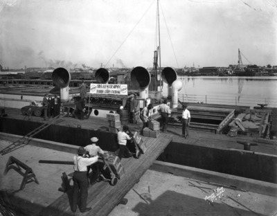 Wooden crates of citrus stacked high and being loaded onto a barge at a waterfront channel.